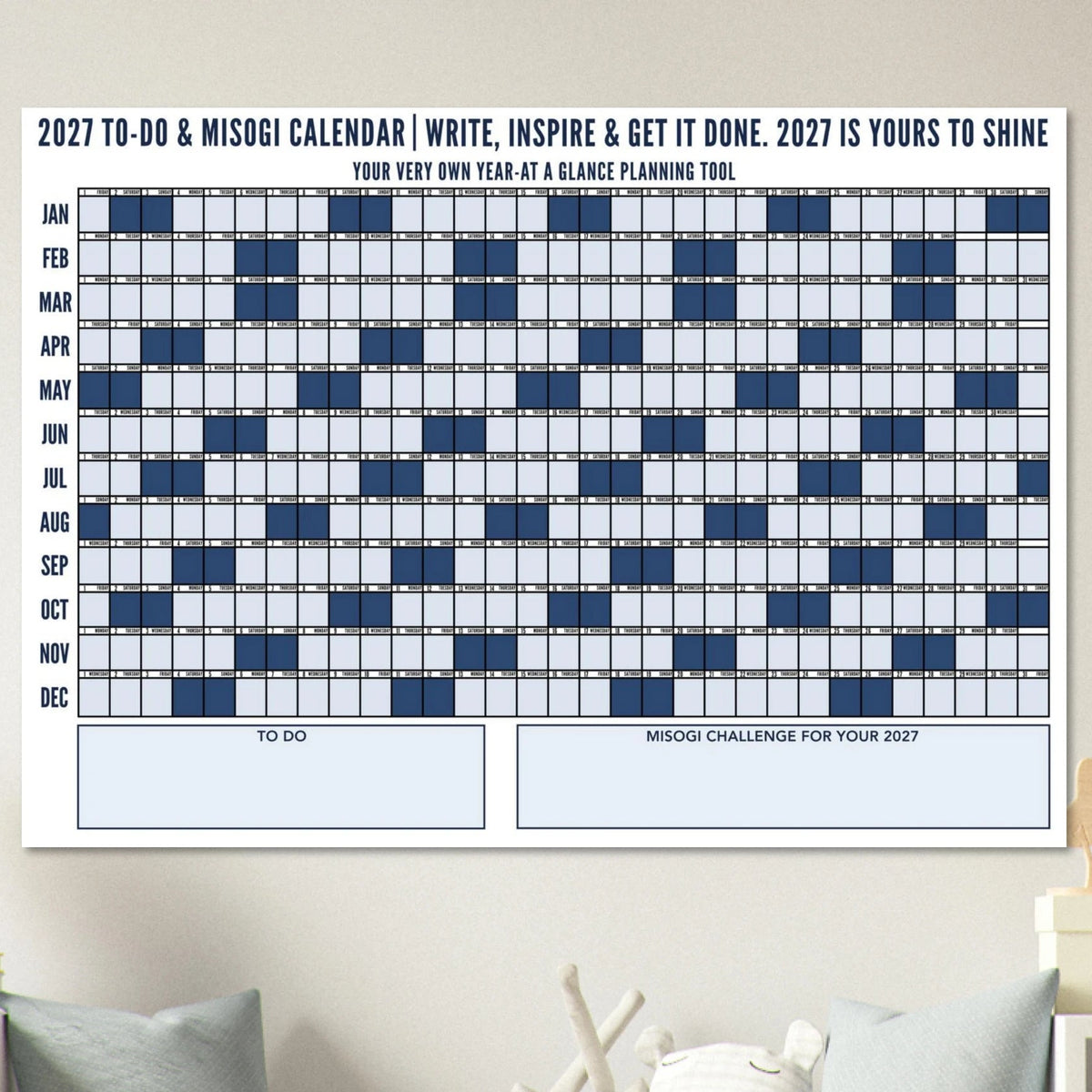 A 2027 To-Do & Misogi Wall Calendar poster displayed on a wall above a green sofa in a styled living room setting.