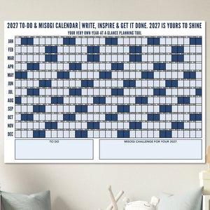A 2027 To-Do & Misogi  Wall Calendar poster displayed on a wall above a green sofa in a styled living room setting. 