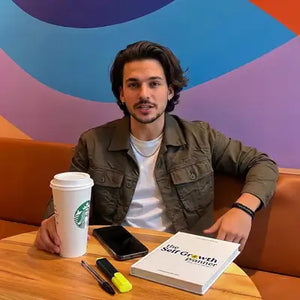 Man sitting at a table with a Starbucks cup, phone, and book against a colorful wall.